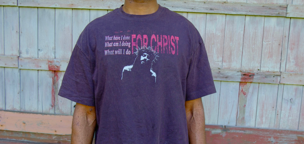 Person wearing a purple t-shirt with text and graphics against a wooden fence background